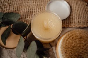 Close-up of a natural cosmetic product alongside eucalyptus leaves and a dry brush, perfect for skincare routines.